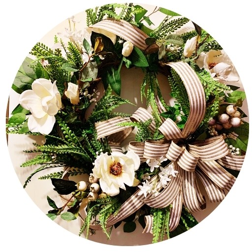 Large round door wreath with greenery and cream colored magnolia flowers all around the wreath. Large tan and cream bow with multiple tails.